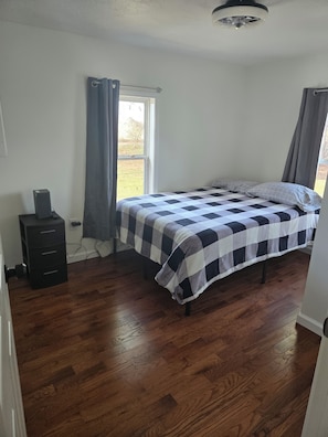 Une chambre à coucher avec un lit, une commode, une fenêtre avec des rideaux et un ventilateur de plafond.