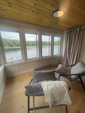 A room with a wooden ceiling, large windows overlooking a lake, and two grey chairs.