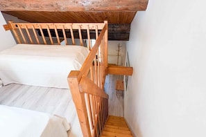 Eine schmale Treppe führt zu einem Schlafzimmer mit einem hölzernen Kopfteil und einer weißen Bettdecke.