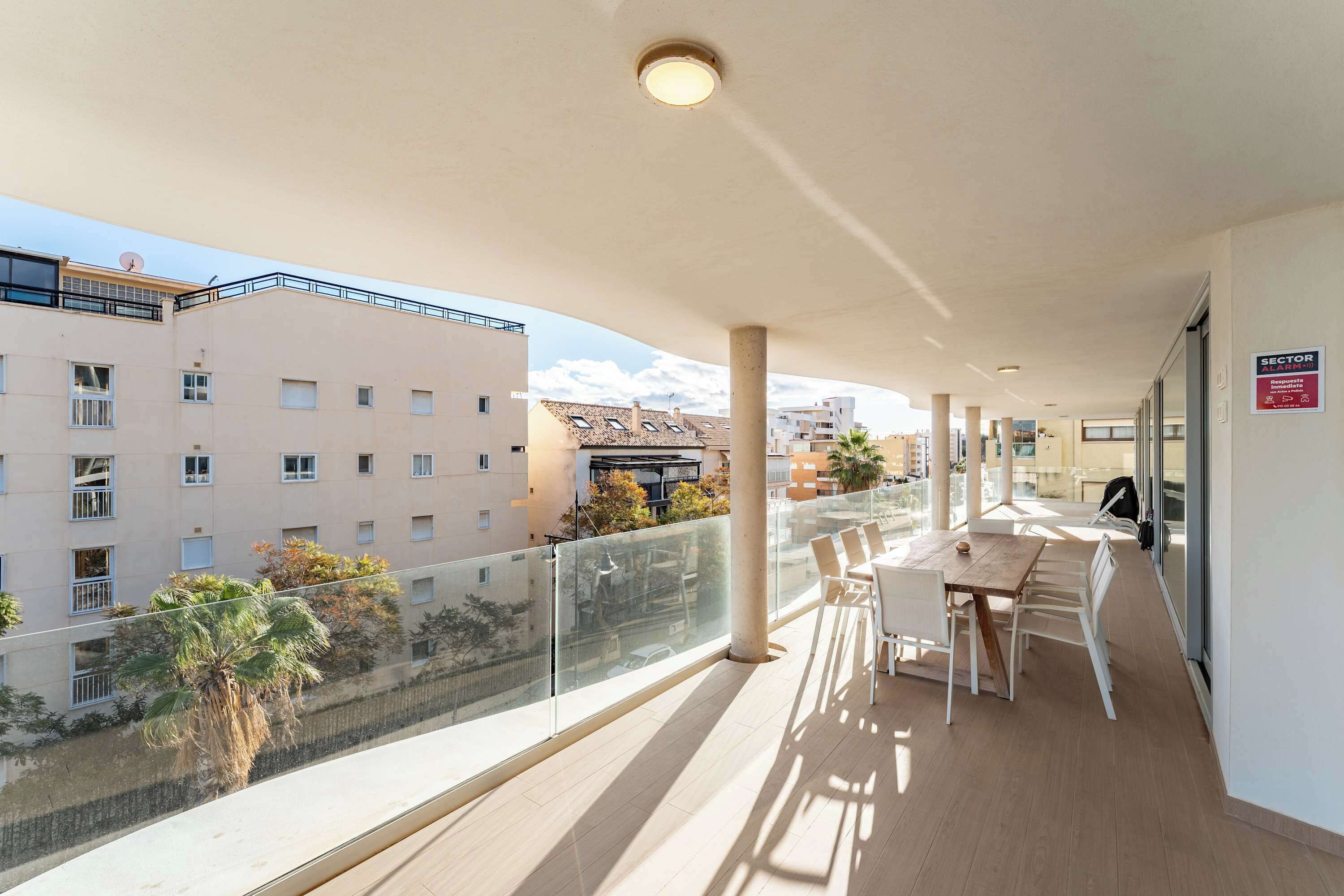 Ein Balkon mit Tisch und Stühlen, einer Glasreling und Blick auf andere Gebäude.
