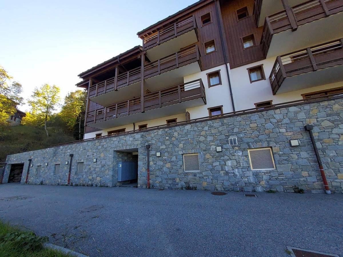 A multi-story building with balconies, stone walls, and a paved entrance area.