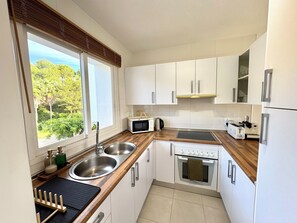 A modern kitchen with white cabinets, a wooden countertop, a built-in oven, a microwave, and a sink. - Fully equipped apartment with beautiful sea, pool and garden view (Las Lagunas de Mijas)