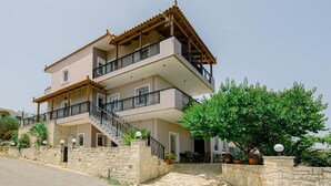 A multi-story building with a balcony on the second floor, a staircase leading to the entrance, and a stone wall surrounding the property.