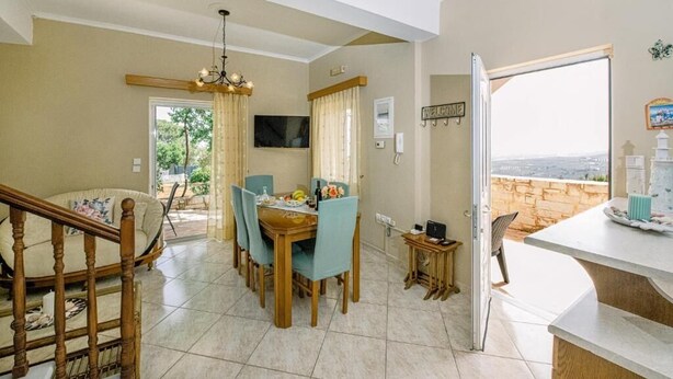A dining area with a wooden table and chairs, a chandelier, and a view of the outdoors through a door.
