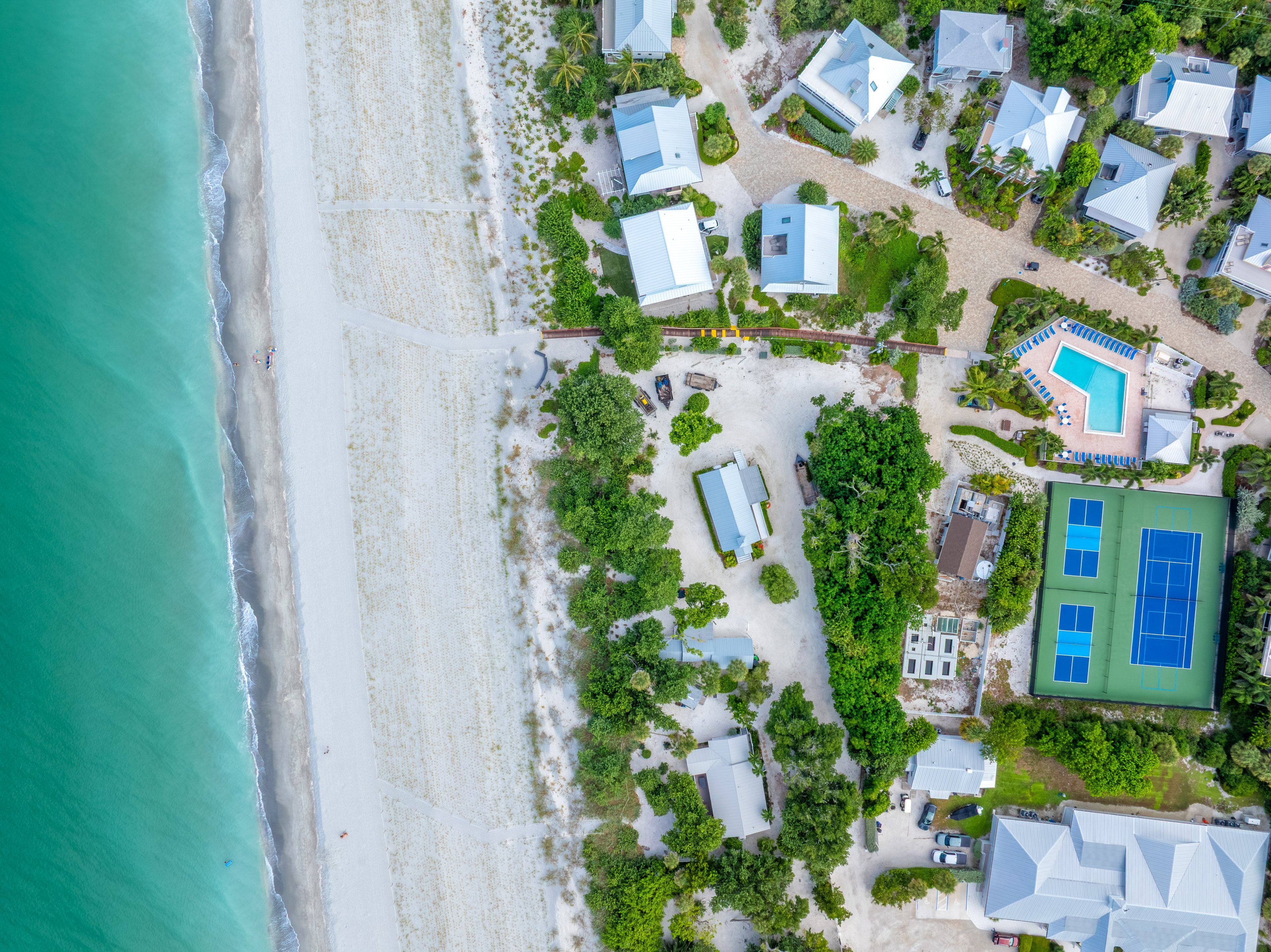 An aerial view of a coastal property with multiple houses, a swimming pool, and a tennis court.
