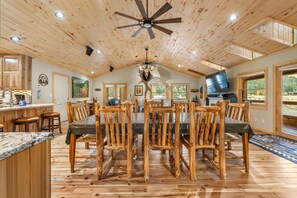 Une salle à manger spacieuse avec un plafond haut, des chaises en bois, une table centrale et un ventilateur de plafond.