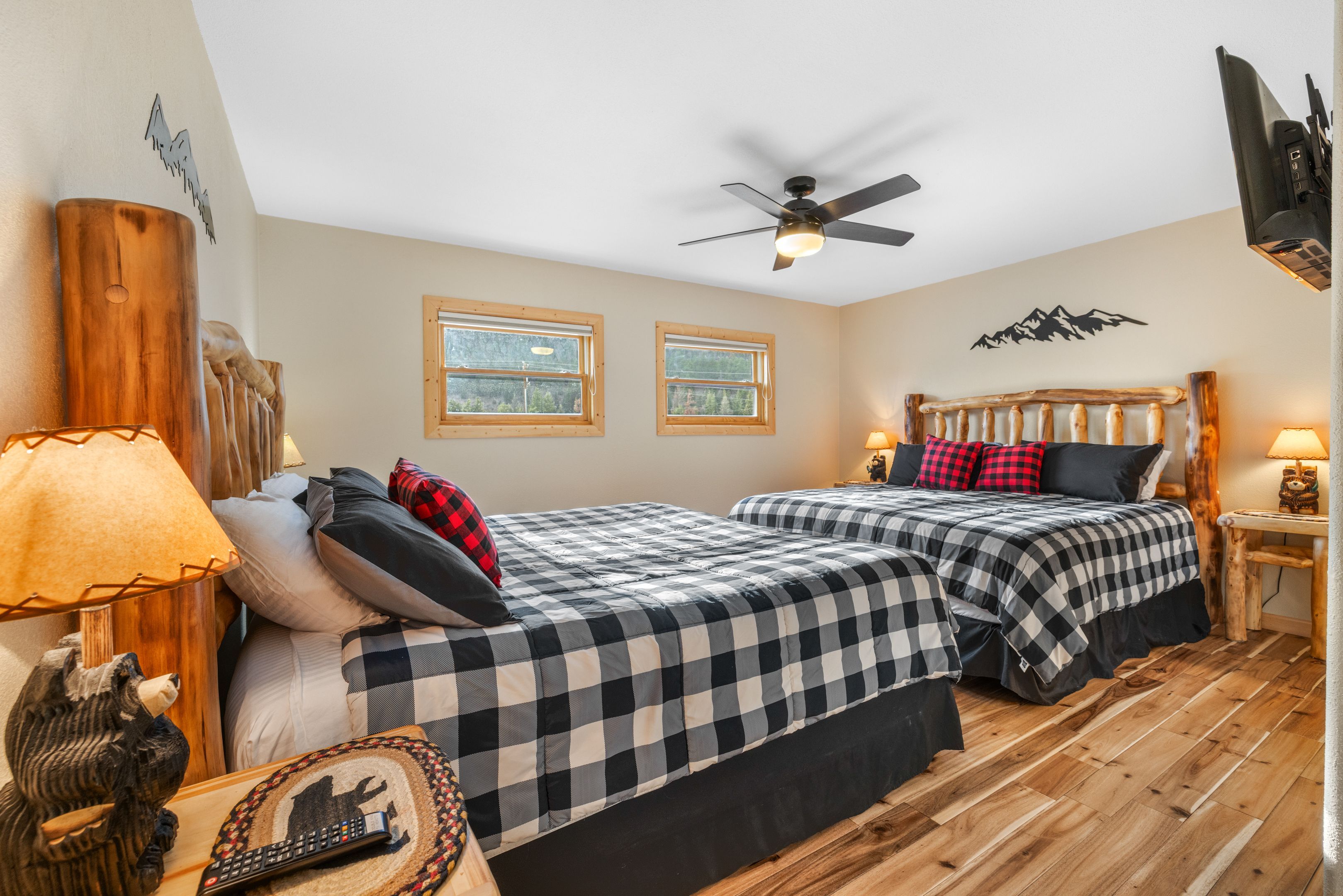 A bedroom with two beds, wooden flooring, a ceiling fan, and a mountain decoration on the wall.