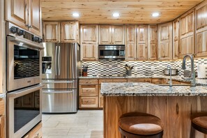 A modern kitchen with wooden cabinets, stainless steel appliances, a granite countertop, and a bar area. - Trout Hunter Cabin- South Fork (South Fork)
