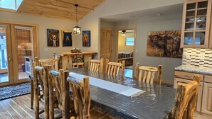 A spacious dining area with a long table and rustic wooden chairs, a wooden ceiling, and artwork on the walls. - Trout Hunter Cabin- South Fork (South Fork)