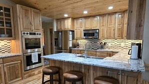 A modern kitchen with wooden cabinets, stainless steel appliances, and a marble countertop. - Trout Hunter Cabin- South Fork (South Fork)