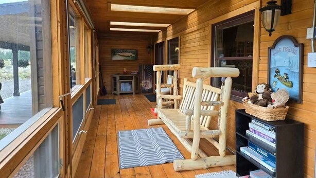 A wooden cabin with a porch, a wooden bench, a wall-mounted lamp, and a framed picture of a boat. - Trout Hunter Cabin- South Fork (South Fork)