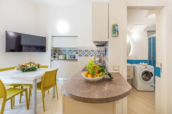 A modern kitchen with a dining area, a washing machine, and a flat-screen TV.