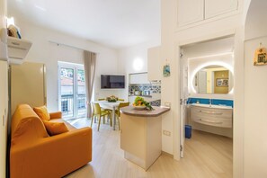 A modern living room with a sofa, a dining area with chairs and a table, a kitchen with a microwave, and a bathroom with a sink and mirror.