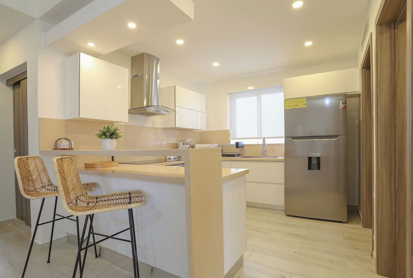 A modern kitchen with a central island, bar stools, stainless steel appliances, and recessed ceiling lighting.