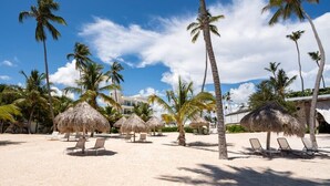 Une plage avec des parasols en chaume, des palmiers et des chaises longues.
