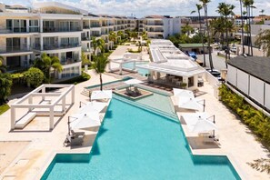 A resort with a central swimming pool, multiple balconies, and palm trees. - Premier 2 Bedrooms Beach Front Condo (Punta Cana)