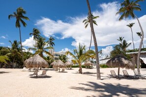 A beach with thatched umbrellas, palm trees, and sun loungers. - Premier 2 Bedrooms Beach Front Condo (Punta Cana)