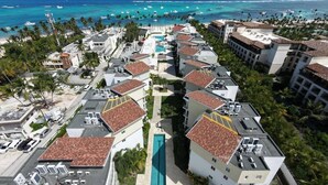 Un complejo turístico con varias edificaciones, una piscina central y vistas al océano.