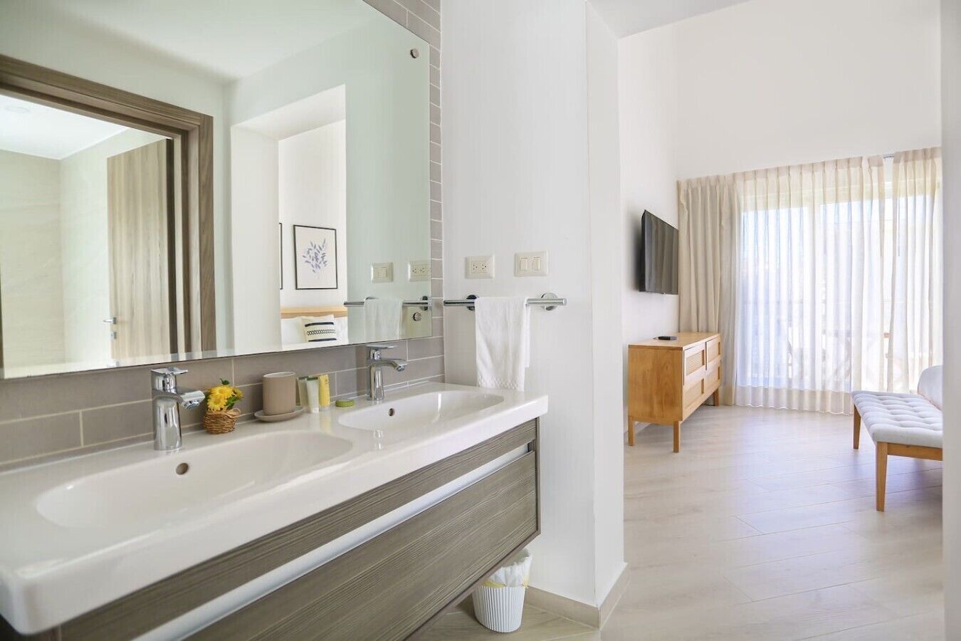 Un baño moderno con dos lavamanos, un espejo grande y un mueble tocador con televisor.