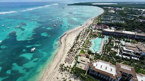 Vista aérea de un complejo turístico frente a la playa, con piscinas y edificios del complejo.