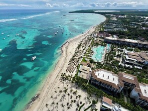 An aerial view of a coastal resort with a beachfront, swimming pools, and resort buildings. - Cozy 2 Bedrooms Garden View Beachfront condo (Punta Cana)