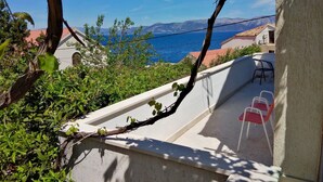 A balcony with a view of the sea, a white building, and a red-roofed house in the background.