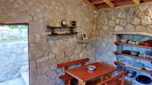 A rustic stone-walled kitchen with wooden beams, shelves with dishes, and a wooden table with a bowl.