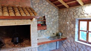 A stone-walled kitchen with a fireplace, wooden beams, and a stone shelf.