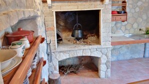A rustic kitchen with a stone fireplace, wooden shelves, and a tiled roof.