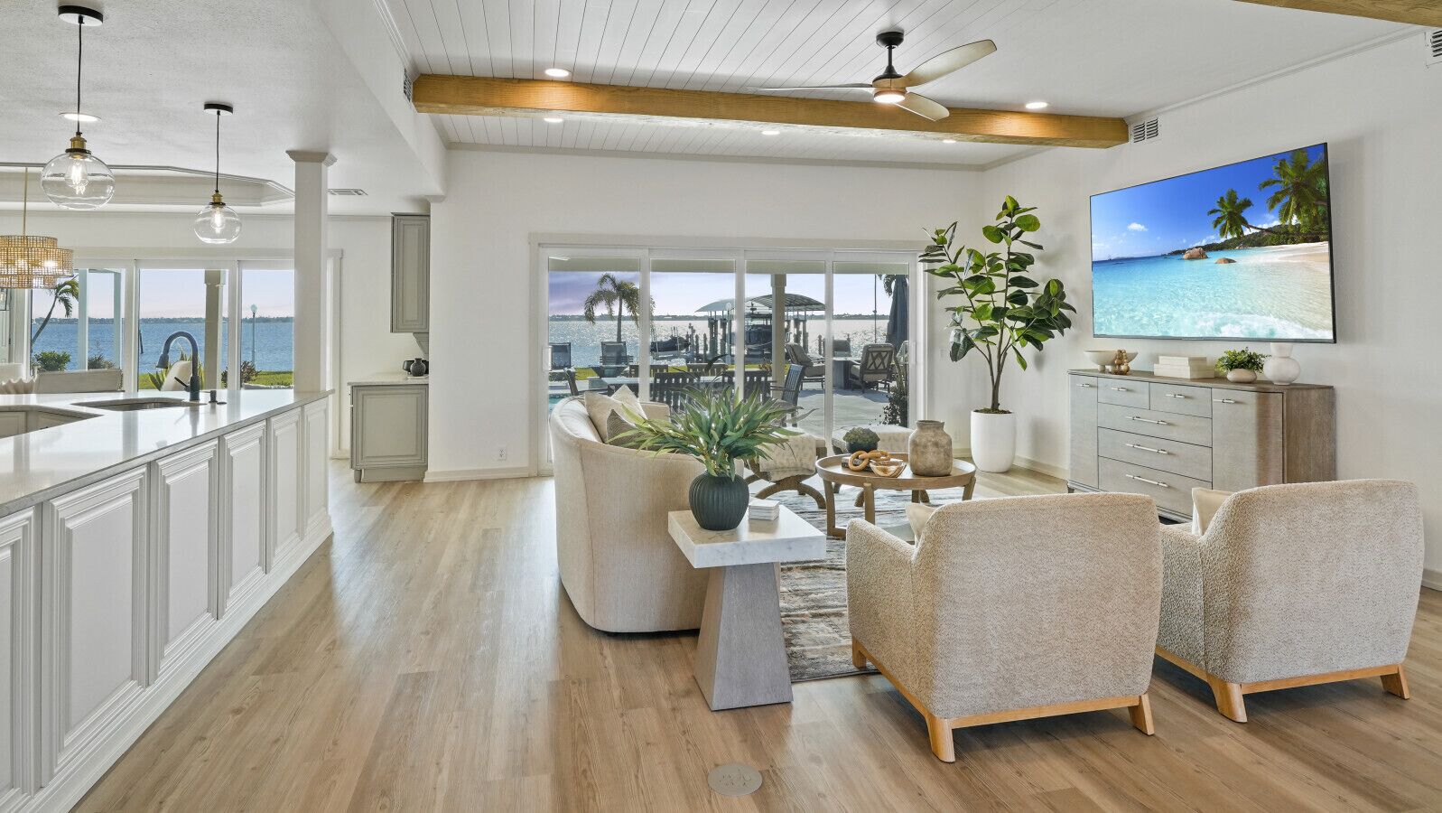 A spacious living area with a view of the sea, a dining table with chairs, and a television on the wall.