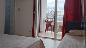 A hotel room with two beds, a TV mounted on the wall, a sliding glass door to a balcony with a chair, and a view of the outdoors. - Comfort Studio Apartment with Sea View and Terrace (Sutomore)