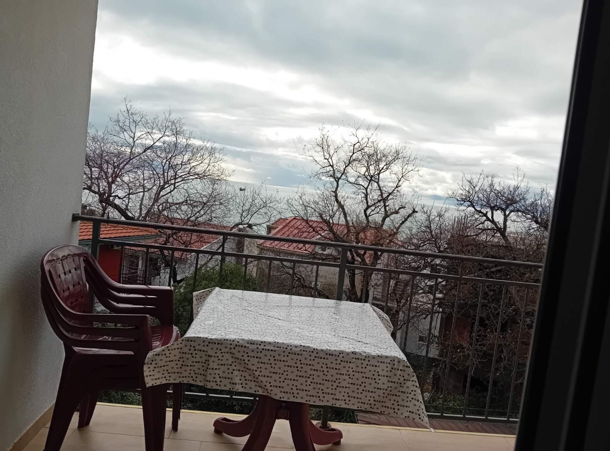 A balcony with a table and chairs, overlooking a residential area with trees and buildings.