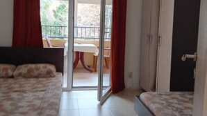 A bedroom with two beds, a balcony with a table and chairs, and a wardrobe. - Classic Triple Room with Mountain View, Loggia and Shared Bathroom (Sutomore)