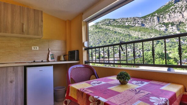 A compact kitchen with a refrigerator, a small sink, and a window overlooking a mountainous landscape. - Classic Triple Room with Mountain View, Loggia and Shared Bathroom (Sutomore)