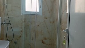 A glass-enclosed shower stall with a marble wall, a small window, and a toilet visible to the left. - Classic Triple Room with Mountain View, Loggia and Shared Bathroom (Sutomore)
