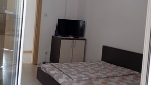 A bedroom with a bed, a television on a stand, and a door leading to another room. - Classic Triple Room with Mountain View, Loggia and Shared Bathroom (Sutomore)