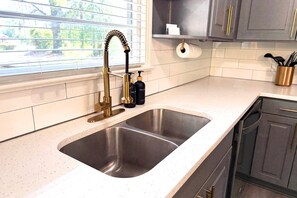 A kitchen with a double stainless steel sink, a gold faucet, and a window with blinds.