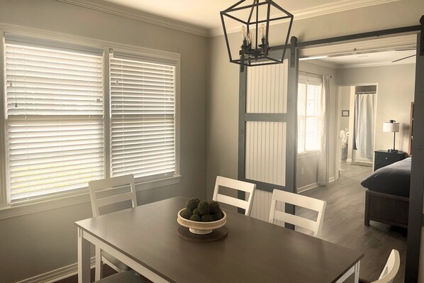 A dining area with a table, chairs, and a bowl of food. There is a window with blinds and a door leading to another room.