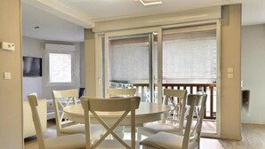 A dining area with a round table and four chairs, a television on the wall, and a sliding glass door leading to an outdoor balcony. - 3 bedrooms with elevator parking hyper center Trouville (Trouville-sur-Mer)