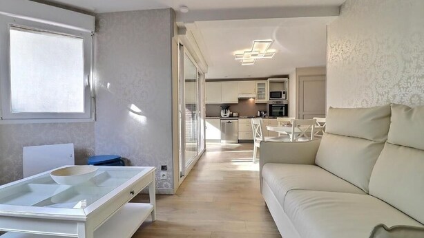 A modern living room with a sofa, a glass-top table, and a kitchen in the background. - 3 bedrooms with elevator parking hyper center Trouville (Trouville-sur-Mer)