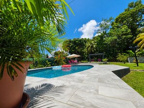 A swimming pool with a tiled deck, surrounded by lush greenery and a clear blue sky. - Tropical Villa - Comfort and Relaxation (Petit-Bourg)