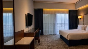 A hotel room with a bed, a desk, a television, and a large window with curtains. - ROSEMARY HOTEL  (Taif)