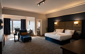 A hotel room with a bed, a desk, a chair, a sofa, a TV, and a view of the outdoors.