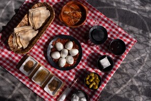 Una mesa con alimentos, entre ellos pan, huevos, aceitunas y salsas, sobre un mantel a cuadros.