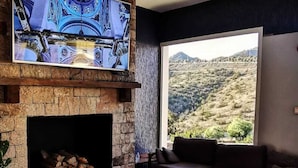 A living room with a stone fireplace, leather sofas, a coffee table, and a large window with a view of a hilly landscape. - ROSEMARY HOTEL  (Taif)