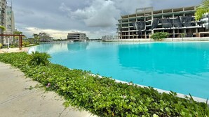 En stor swimmingpool med en omgivende gangsti, ved siden af en flereetagers bygning med en overdækket parkeringskælder.