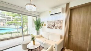 En moderne stue med en hvid sofa, et rundt sofabord og et stort vindue med udsigt over en pool.