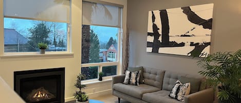A modern living room with a fireplace, a grey sofa, and a large abstract painting on the wall.