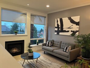 A modern living room with a fireplace, a grey sofa, and a large abstract painting on the wall. - Gorgeous 3-bedroom home in charming Central Lonsdale (North Vancouver)