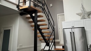 Eine moderne Küche mit integriertem Treppenhaus, Edelstahlgeräten und einer Pendelleuchte.
